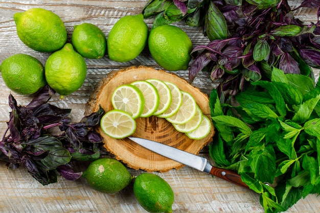 Lemons with basil bunches, knife on wooden and cutting board, flat lay.