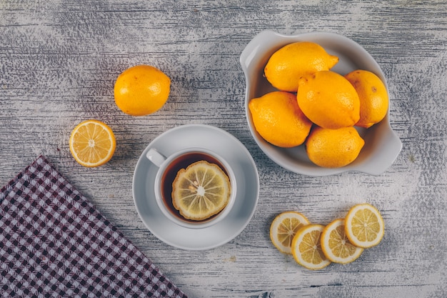 Free photo lemons with cloth, tea and slices in a bowl and on gray wooden background, top view.