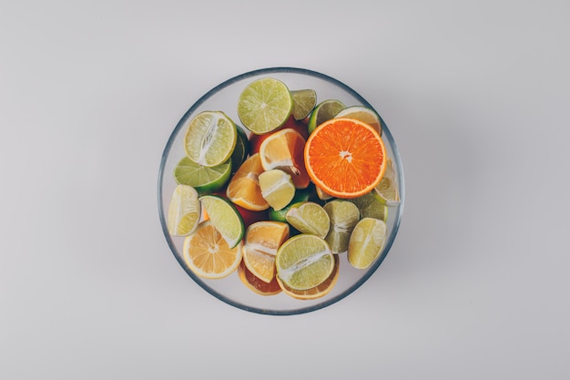 Lemons with green lemons and orange in a bowl on white background, top view.