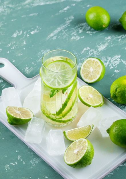 Free photo lemons with ice cubes, lemonade high angle view on plaster and cutting board