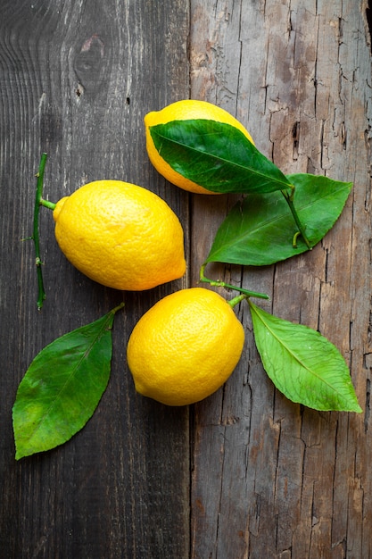 Free photo lemons with leaves on dark wooden background, top view. vertical