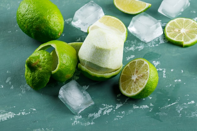 Lemons with peel, ice cubes on plaster, high angle view.