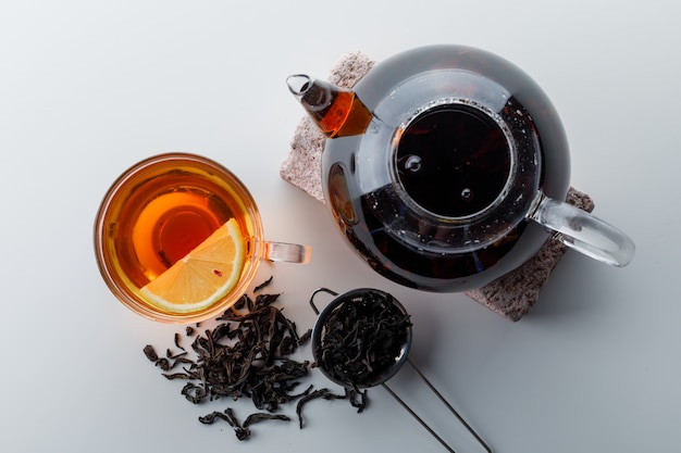 Lemony tea with teapot on brick, strainer, dry tea in a cup on white gradient surface, top view