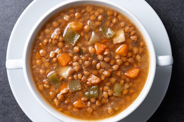 Lentil soup with vegetables in bowl on black background