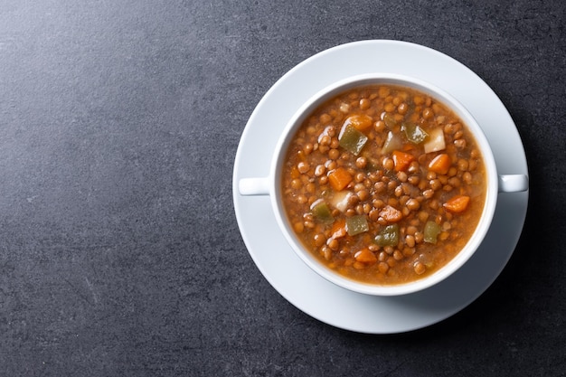 Lentil soup with vegetables in bowl on black background