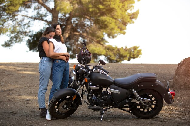 Lesbian couple embracing near motorcycle while on a road trip