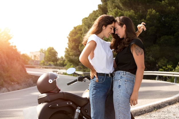 Lesbian couple embracing near motorcycle while on a road trip