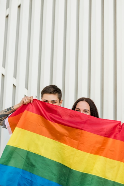 Free photo lesbian couple hiding behind lgbt flag