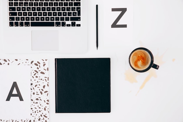 Letter a and z; pencil; diary; laptop and spilled coffee cup on white backdrop