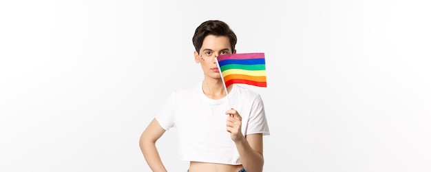 Lgbtq community attractive queer man with flitter on face waving pride rainbow flag and looking at c