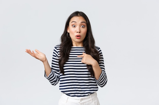 Lifestyle, beauty and fashion, people emotions concept. Shocked and surprised girl pointing at herself and shrugging as was picked or chosen, standing white background.