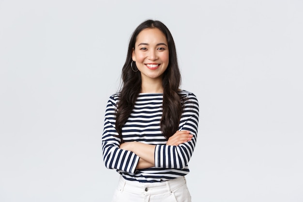 Free photo lifestyle, beauty and fashion, people emotions concept. young asian female office manager, ceo with pleased expression standing over white background, smiling with arms crossed over chest.