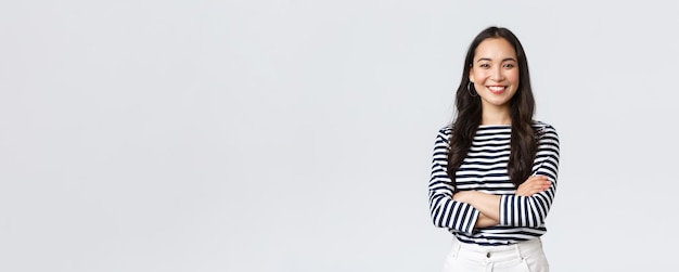 Lifestyle beauty and fashion people emotions concept Young asian female office manager CEO with pleased expression standing over white background smiling with arms crossed over chest