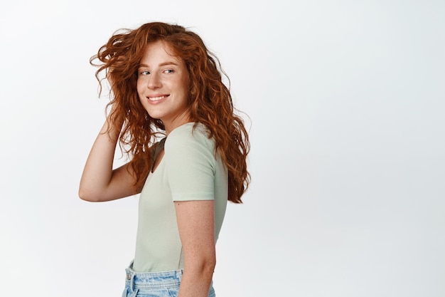 Free photo lifestyle and people cute candid girl with red curly hair and freckles playing with haircut and smiling happy at camera standing in tshirt over white background