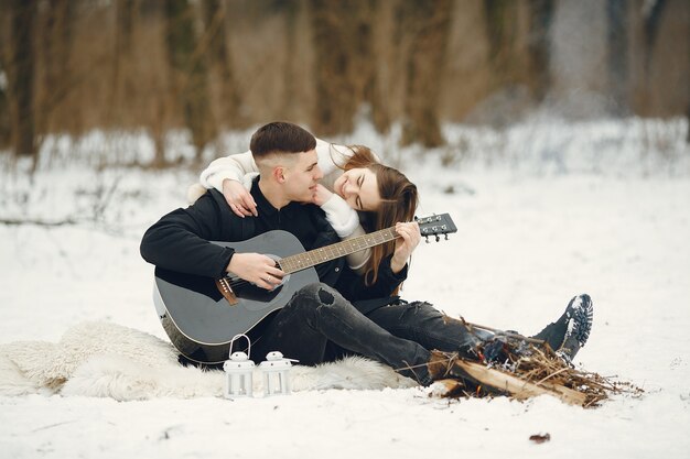 Lifestyle shot of couple sitting in snowy forest. People spending winter vacation outdoors. Couple wit a guitar.