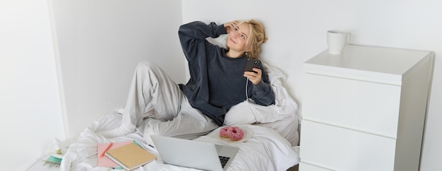 Free photo lifestyle and weekend concept young smiling woman relaxing at home lying in bed with cup of tea and