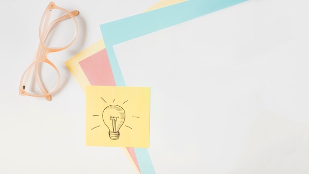 Light bulb drawn on adhesive note over the card paper and eyeglasses on white background