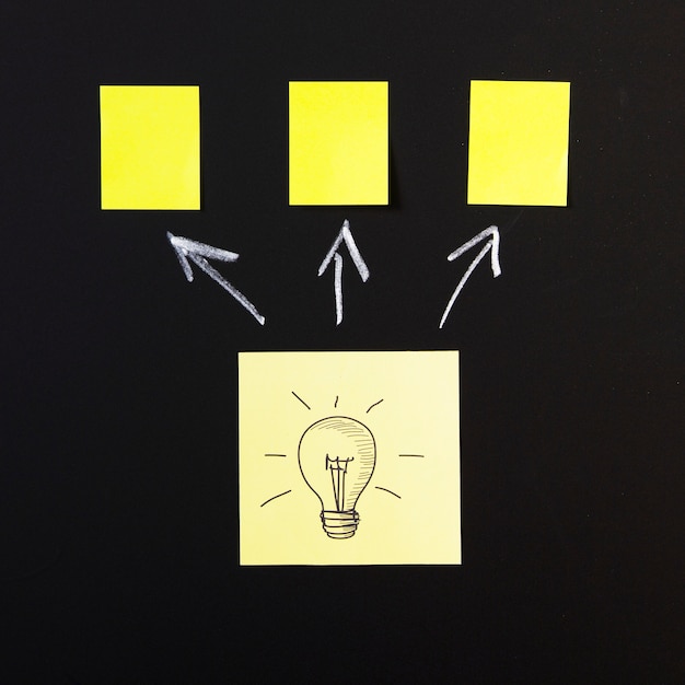 Free Photo light bulb icon on sticky note with arrows drawn on blackboard