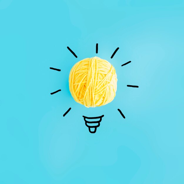 Light bulb made with yellow ball of yarn on blue backdrop