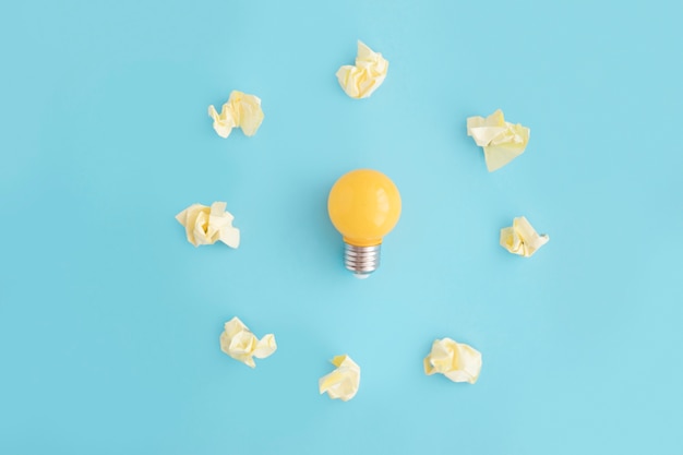 Free Photo light bulb surrounded with yellow crumpled paper on blue background