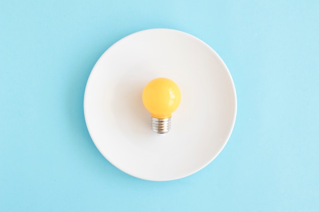 Free Photo light yellow bulb on white dish over the blue backdrop