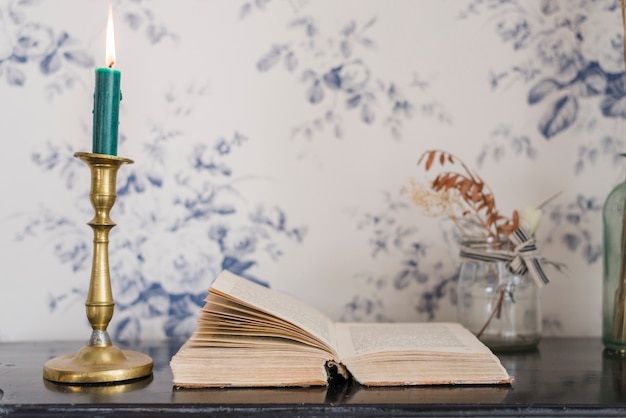 Lighted candle over the candlestick holder and an open book on desk against wallpaper