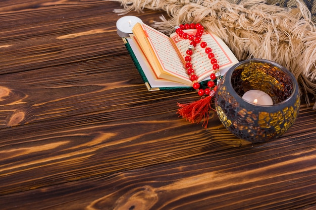 Free Photo lighted candle holder; kuran and red prayer beads on wooden desk