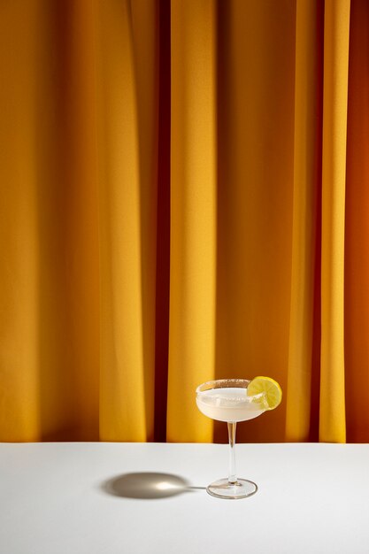 Lime cocktail in saucer glass on white table against yellow curtain