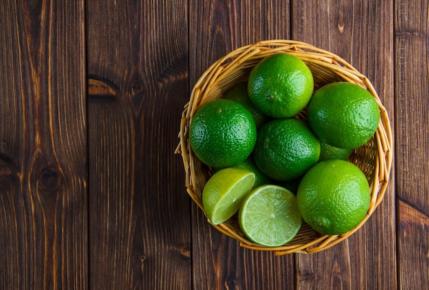 Limes in a wicker basket on wooden table. flat lay.