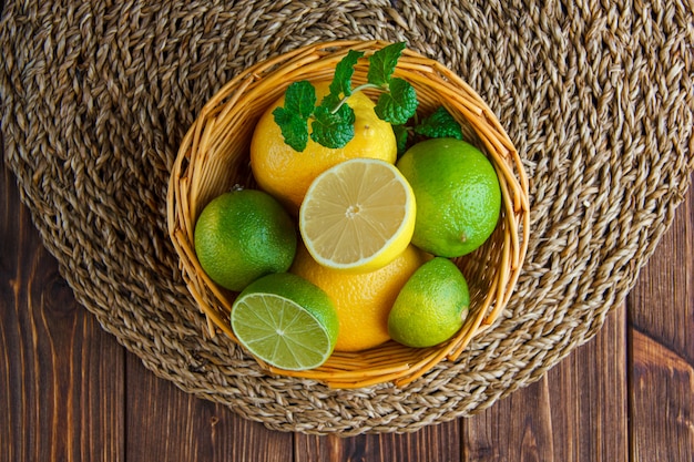 Free photo limes with lemons, herbs in a wicker basket on wooden table