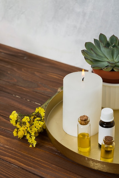 Free photo limonium flower with white large lighted candle and essential oil bottle on wooden desk