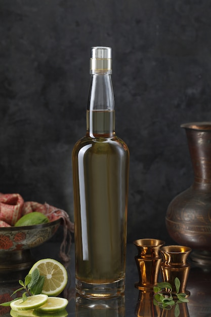 Liquor bottle with mini goblets, vase, lemon, scarf and mint leaves