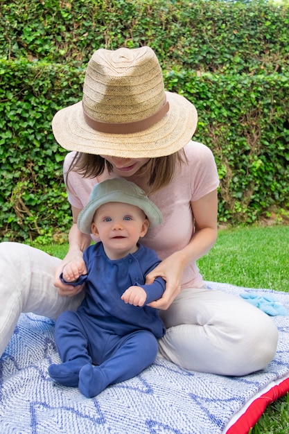 Free photo little baby girl sitting on plaid with young mom in hat