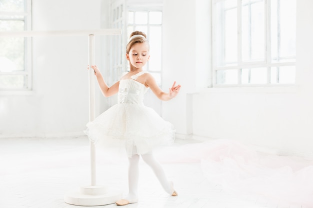 Little ballerina girl in a tutu. Adorable child dancing classical ballet in a white studio.