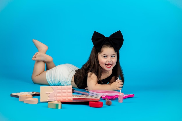 Little beautiful smiling girl with a funny face in a striped yellow dress posing on a blue background in studio