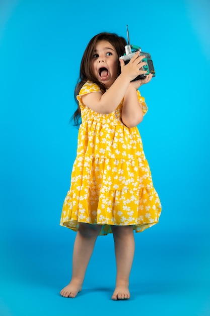 Little beautiful smiling girl with a funny face in a striped yellow dress posing on a blue background in studio