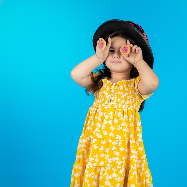 Little beautiful smiling girl with a funny face in a striped yellow dress posing on a blue background in studio