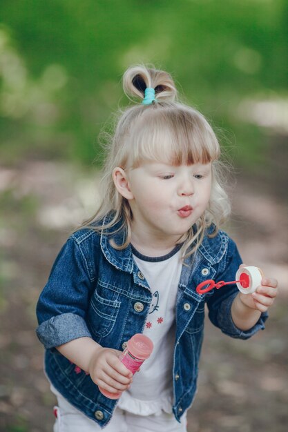 Little blond girl blowing by a pompous and making bubbles