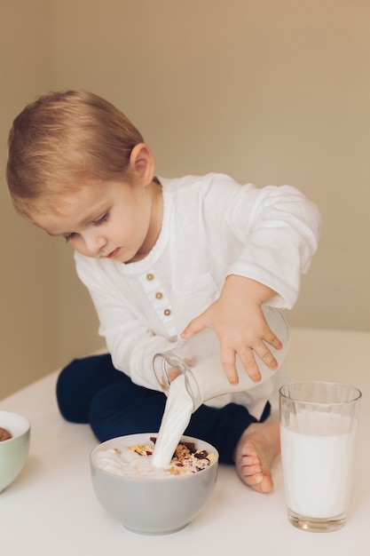 Little boy adding milk to cereals