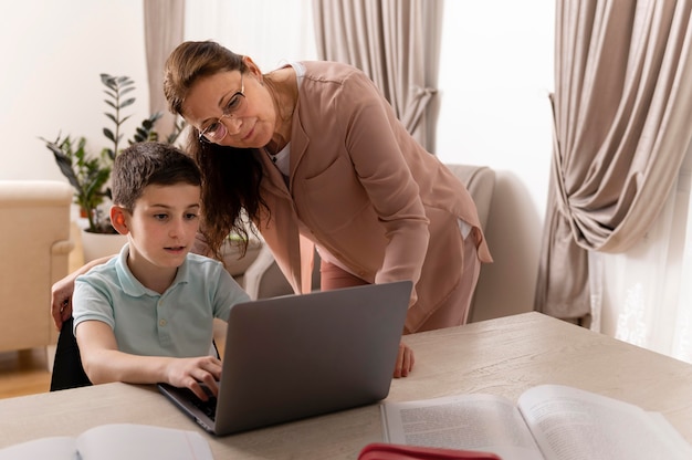 Little boy doing homework with his grandmother on laptop