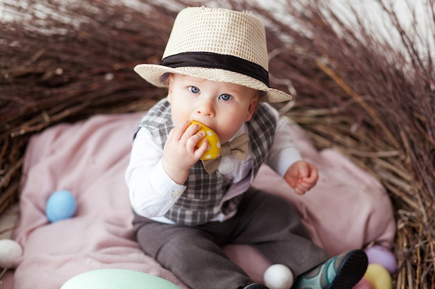 Free photo little boy in hat sitting in nest and eating easter egg.