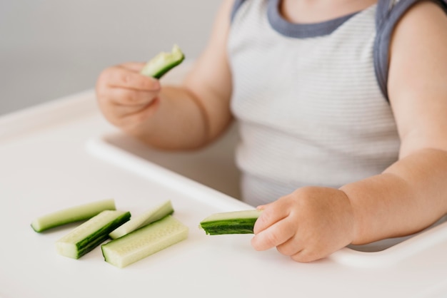 Little boy in highchair holding cucumber pieces