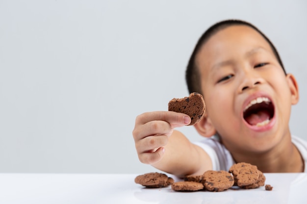 Free photo little boy is holding cookie want to eat at table on white wall.