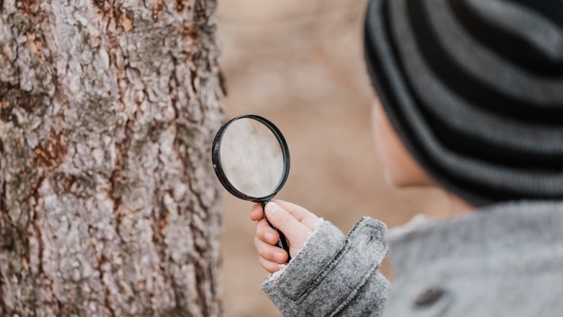 Free photo little boy looking through a magnifier outdoors