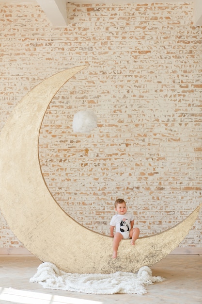 Free photo little boy posing on big moon toy with loft brick wall background