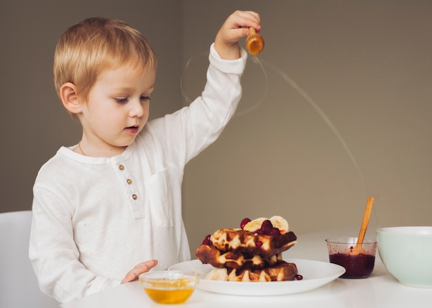 Free Photo little boy putting honey on waffle