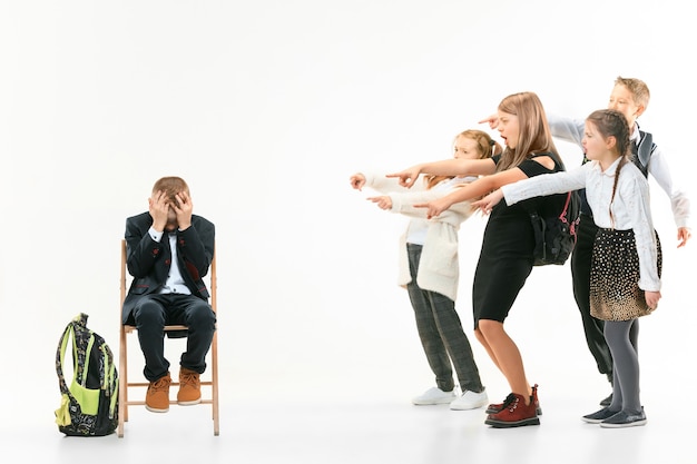 Little boy sitting alone on chair and suffering an act of bullying while children mocking