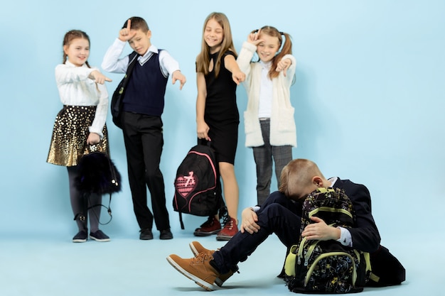 Little boy sitting alone on floor and suffering an act of bullying while children mocking