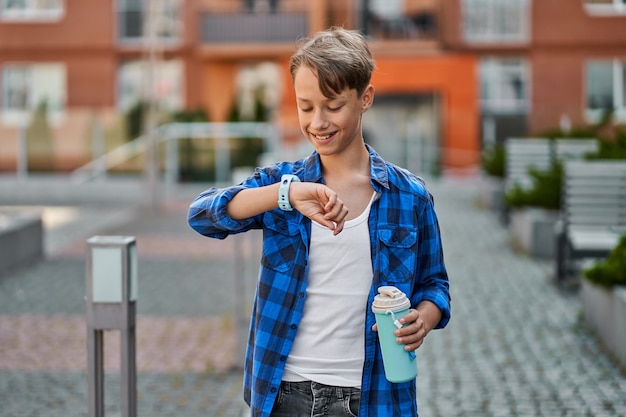 Little boy speaking by blue smartwatch and drink tea near school.