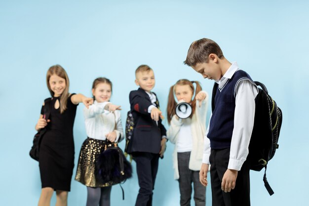 Little boy standing alone and suffering an act of bullying while children mocking in the wall